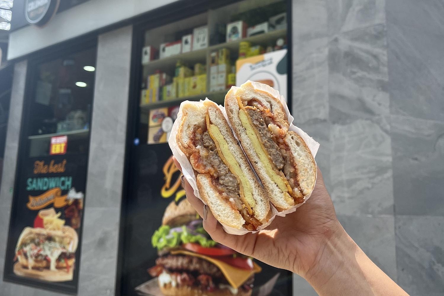 Person holding Plantega plant-based sandwich in front of corner store
